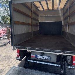 Transport- Przemysław Goździk - Pusta przestrzeń ładunkowa busa z otwartą klapą załadunkową. Widoczna tablica rejestracyjna i sylwetka osoby na zewnątrz. Dostępne światło dzienne.