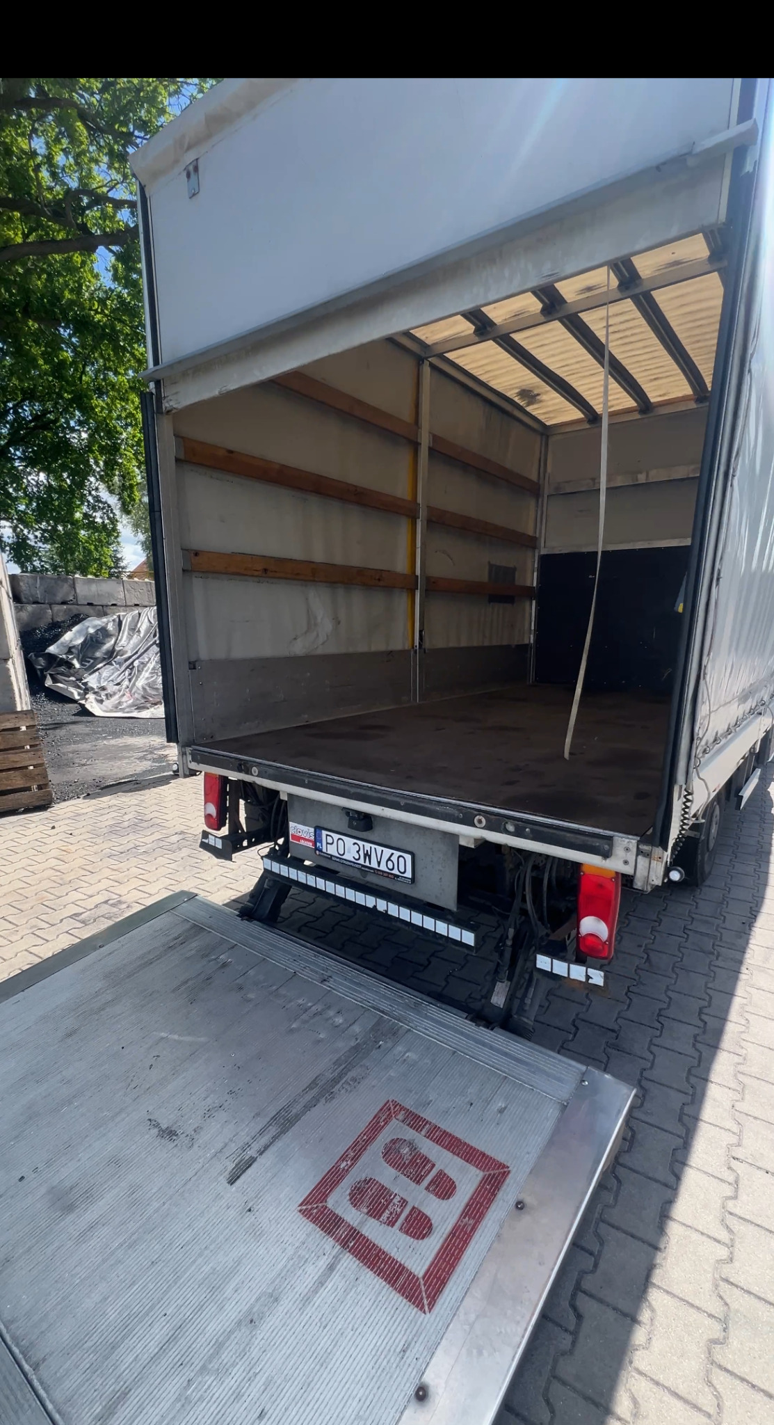 Otwarta paka busa z windą załadowczą, widok z tyłu. Na windzie czerwony znak z odciskiem stóp. Widoczna tablica rejestracyjna z Polski.