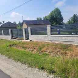 POZBRAM USŁUGI ŚLUSARSKO - SPAWALNICZE - PAWEŁ POZNAŃSKI - Nowoczesne ogrodzenie posesji z szarymi, poziomymi panelami i białymi, murowanymi słupkami. Widok na dom w tle, trawa i droga na pierwszym planie.