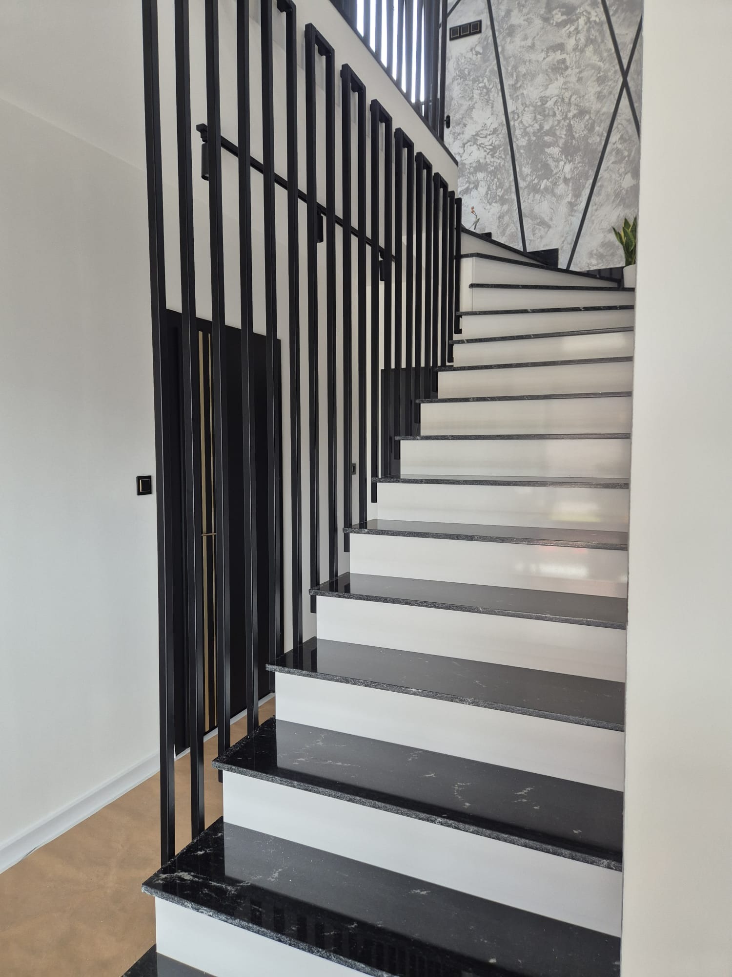 Nowoczesne schody z czarnymi, metalowymi poręczami i marmurowymi stopniami. Minimalistyczny design, jasne ściany i dekoracyjna faktura ściany w tle.