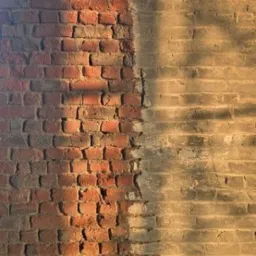 Fragment ceglanej ściany po czyszczeniu, z widocznym podziałem na obszar oczyszczony i nieoczyszczony, różniące się kolorem i strukturą, oświetlony ciepłym światłem.