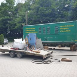 Tortura Rdzy piaskowanie, malowanie proszkowe, konserwacje - Przyczepa z piaskarką ciśnieniową, workiem ścierniwa i wężami na tle zielonego kontenera z hasłami ekologicznymi i informacjami o usługach.