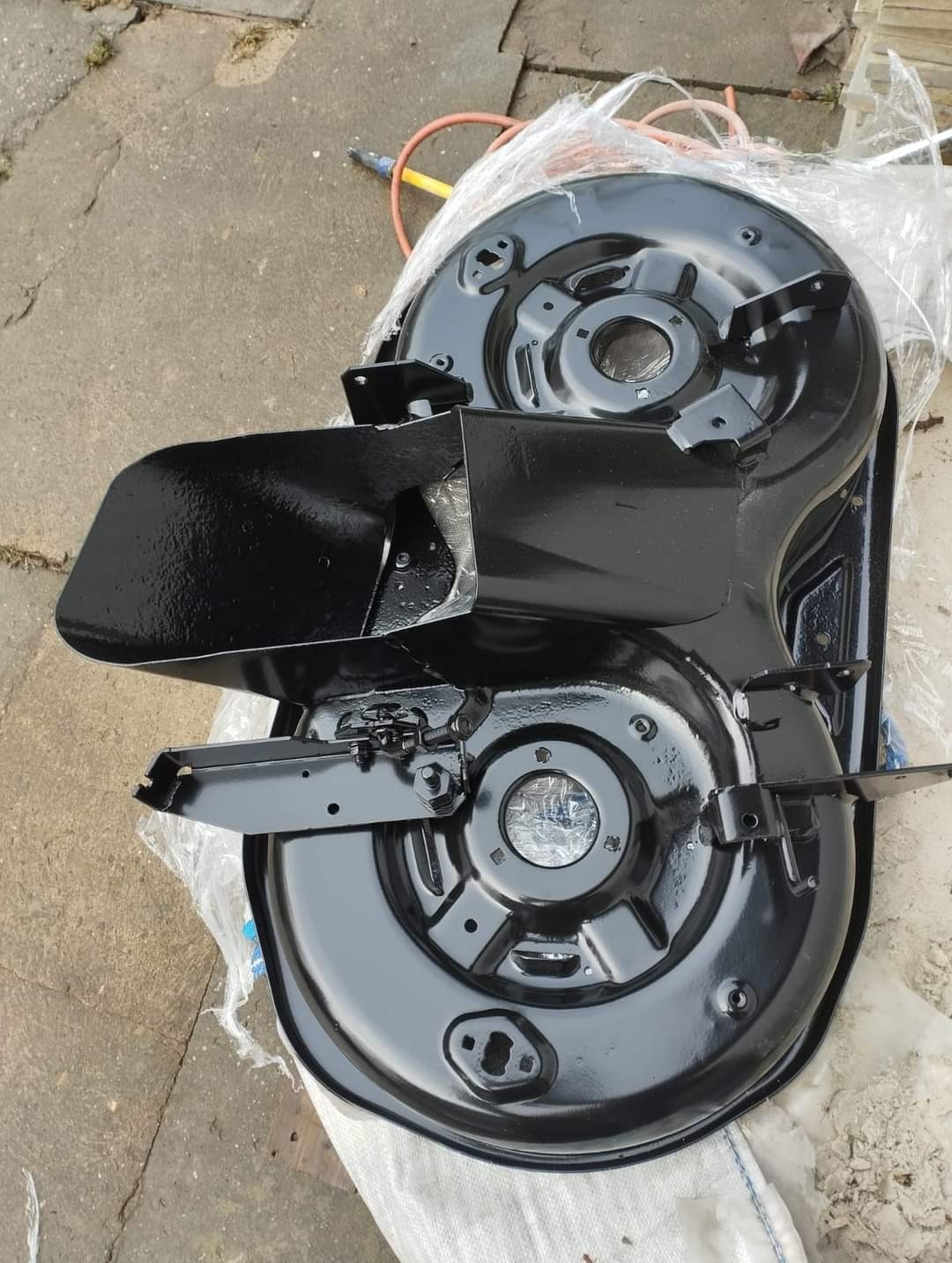 Pompa do kosiarki po renowacji, świeżo pomalowana na czarno, leży na folii ochronnej na betonowym podłożu. Widoczne ślady wcześniejszej korozji pod nową warstwą farby.