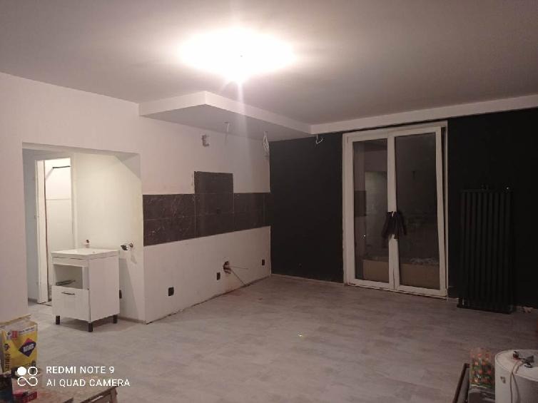 Wnętrze w trakcie prac wykończeniowych: częściowo położone płytki na ścianie, biała szafka umywalkowa, pomalowana na czarno ściana, grzejnik oraz widoczne przewody elektryczne.