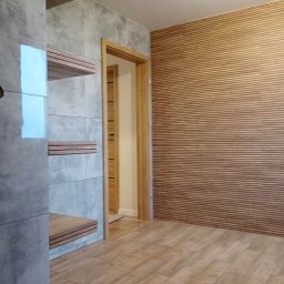 ART-HOUSE - Wykończone wnętrze: ściana z drewnianych paneli, szara ściana z półkami z drewnianych listew i drewniana podłoga imitująca deski.