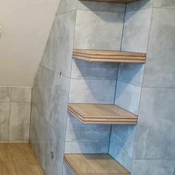 ART-HOUSE - Wykończona łazienka na poddaszu z szarymi płytkami imitującymi beton i drewnianymi półkami wbudowanymi we wnękę