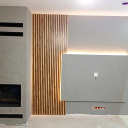 ART-HOUSE - Szary kominek z poziomymi szczelinami, drewniana okładzina ścienna z pionowych listew i podświetlany panel ścienny tworzą nowoczesny design salonu.