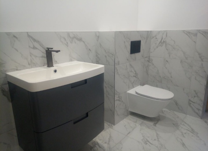 Nowoczesna łazienka w Tuliszkowie z marmurowymi płytkami, podwieszana toaleta i szara szafka z umywalką oraz czarną armaturą.