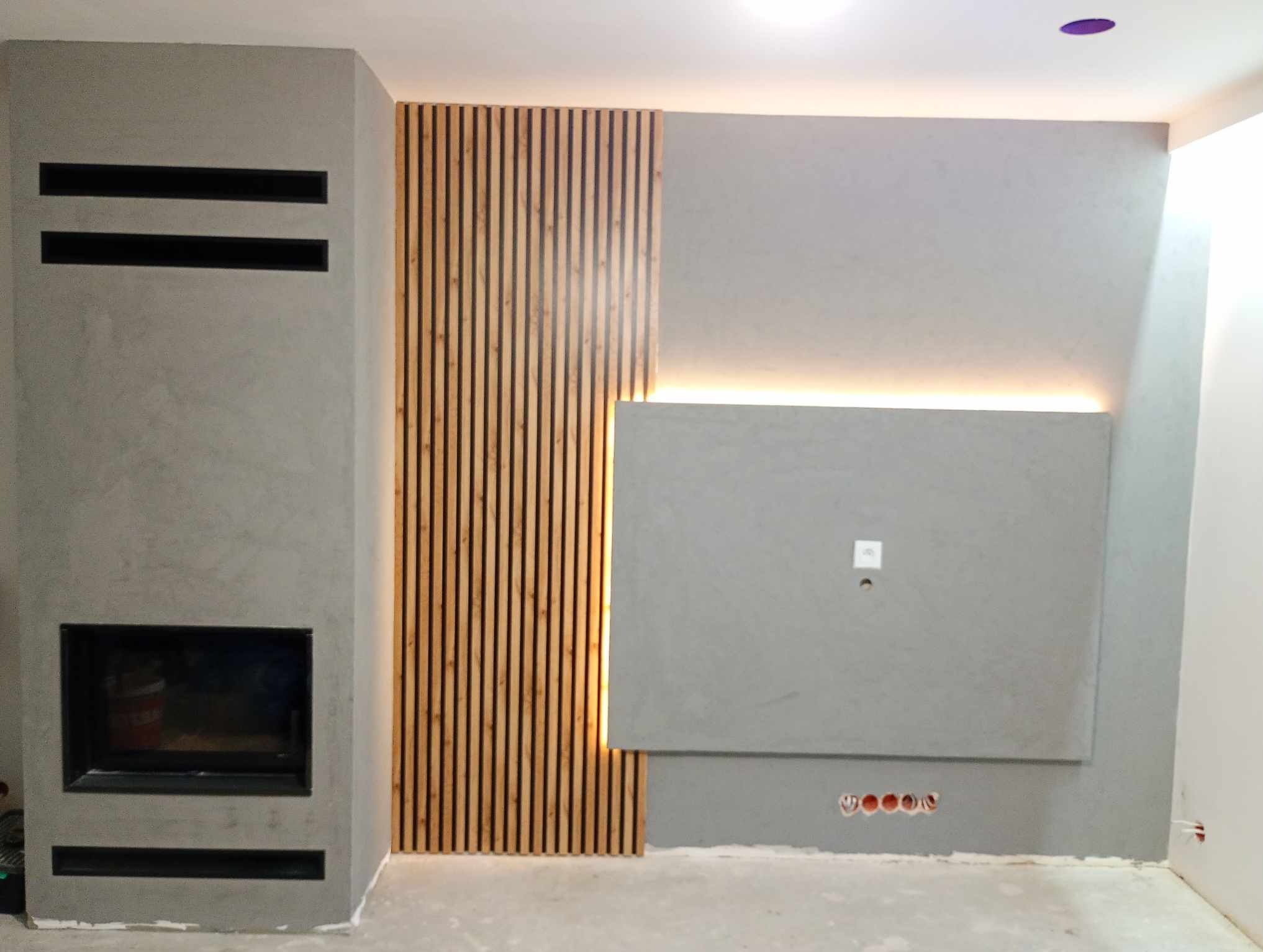 Szary kominek z poziomymi szczelinami, drewniana okładzina ścienna z pionowych listew i podświetlany panel ścienny tworzą nowoczesny design salonu.