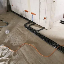 Układanie peszli z kablami elektrycznymi w surowym wnętrzu budynku z bloczków, widoczna skrzynka narzędziowa i odkurzacz przemysłowy.