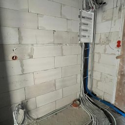 Tomodom Tomasz Turski - Rozdzielnia elektryczna z poprowadzonymi przewodami w surowym wnętrzu. Widoczne kable w peszlach ułożone na podłodze i przy ścianach z betonu komórkowego.