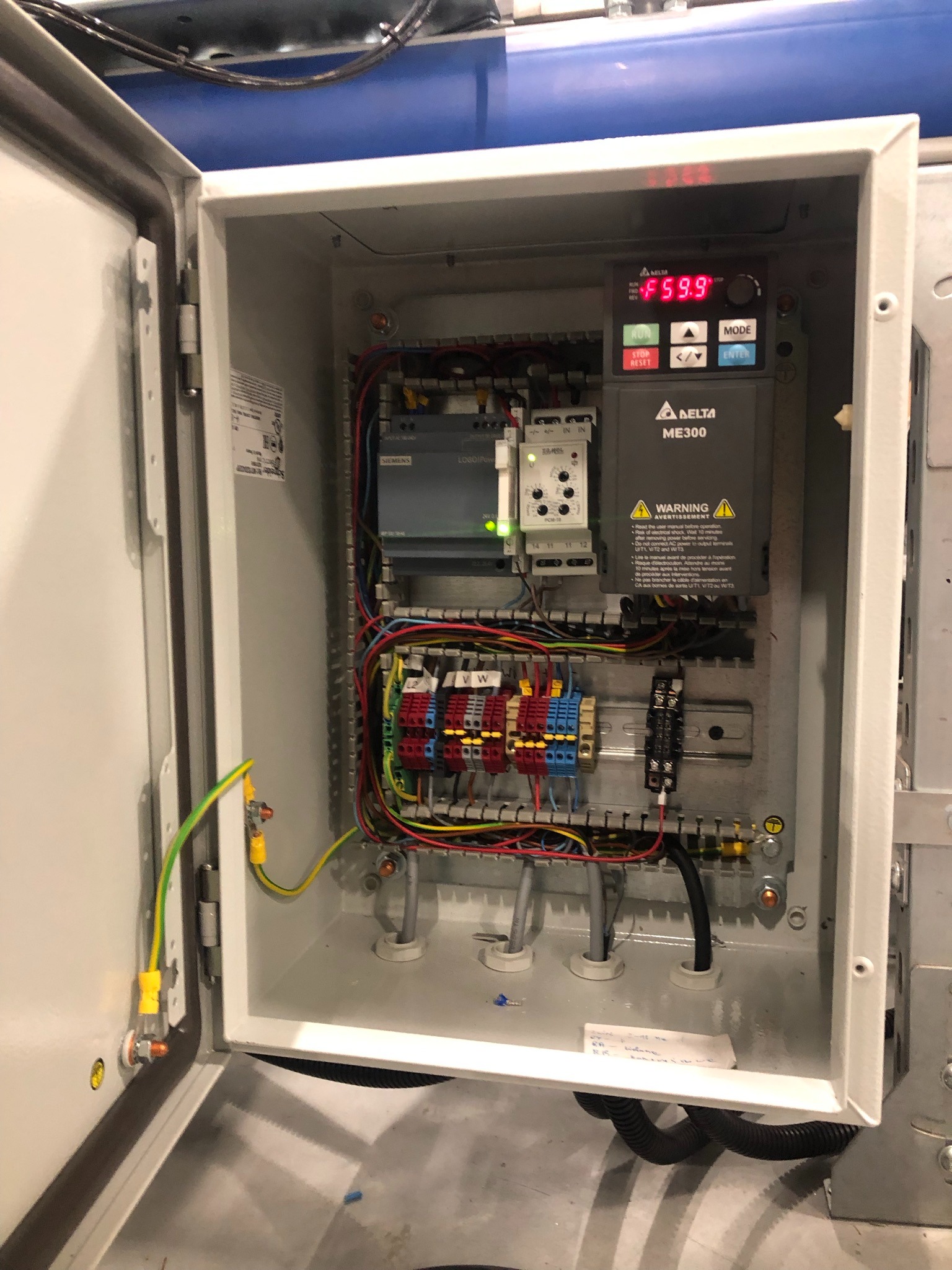 Otwarta szafa sterownicza z zamontowanym falownikiem Delta ME300, modułem Siemens LOGO!, bezpiecznikami, okablowaniem i uziemieniem, widoczny wyświetlacz falownika.
