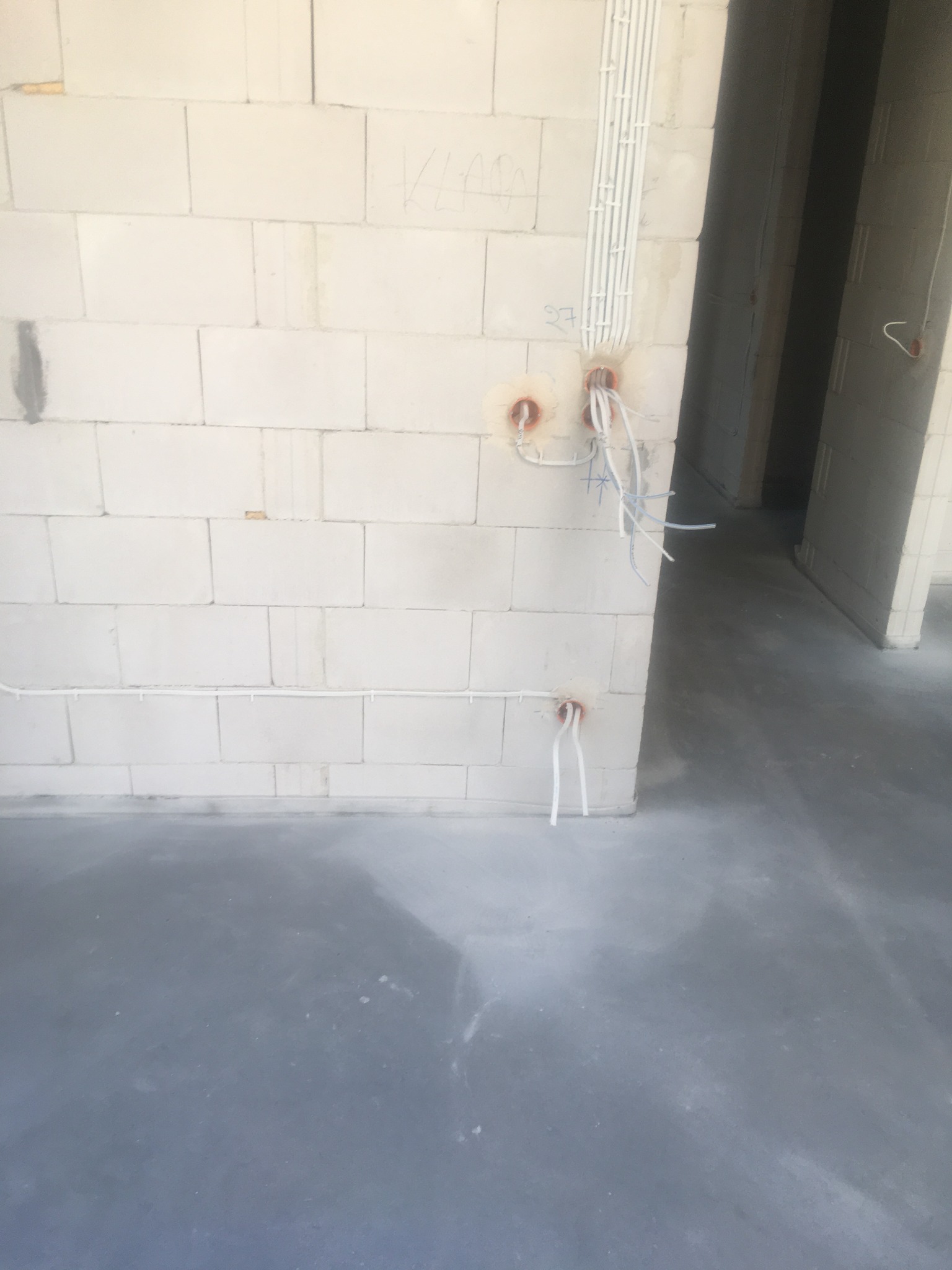 Surowy mur z betonu komórkowego z przygotowanymi otworami i peszlami na przewody elektryczne, widoczne kable, szare wylewki podłogowe w nowym budynku.