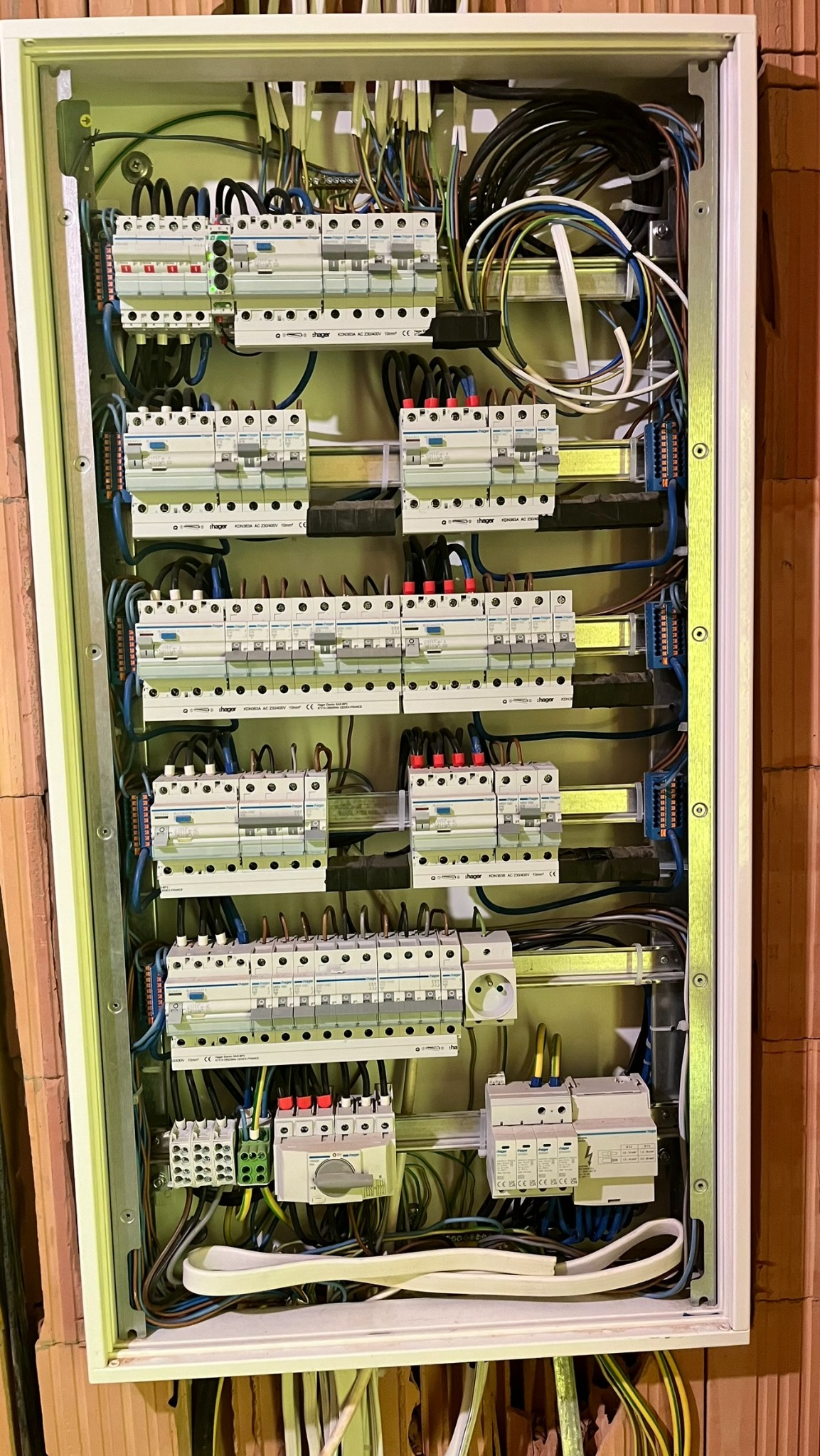 Otwarta skrzynka rozdzielcza z licznymi bezpiecznikami i przewodami, zamontowana na ścianie z cegły.