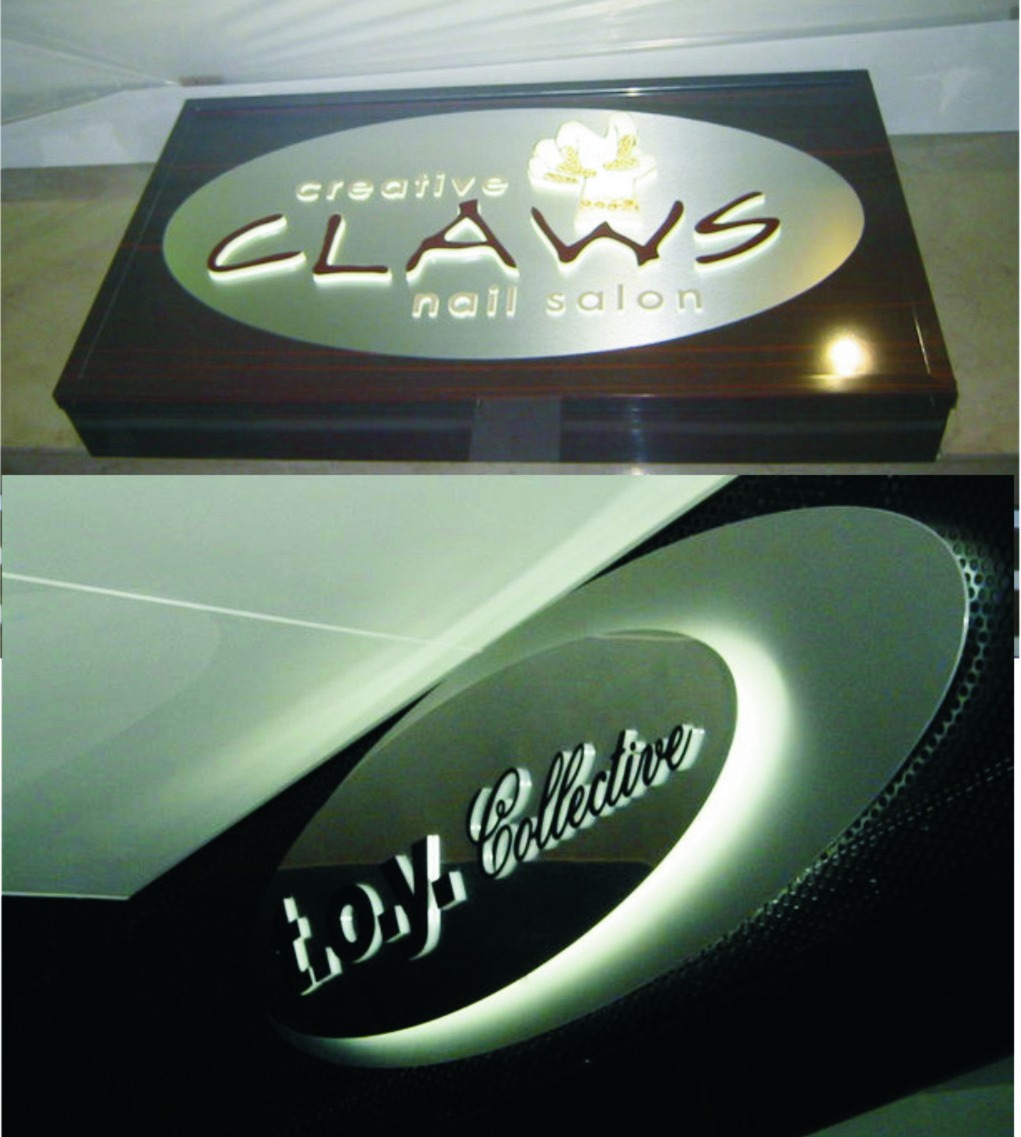 Dwa podświetlane szyldy firmowe w kształcie elipsy: jeden z napisem 'creative CLAWS nail salon' na drewnianej podstawie, drugi z napisem 'Loy Collective' na czarnym tle.
