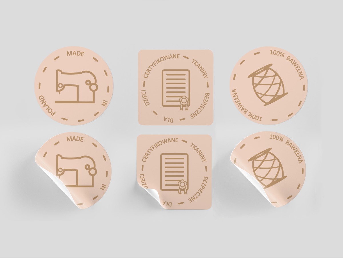 Kolekcja naklejek z motywami krawieckimi i tekstylnymi: maszyna do szycia 'Made in Poland', certyfikat bezpieczeństwa tkanin dla dzieci oraz informacja '100% bawełna', prezentowane przez firmę...