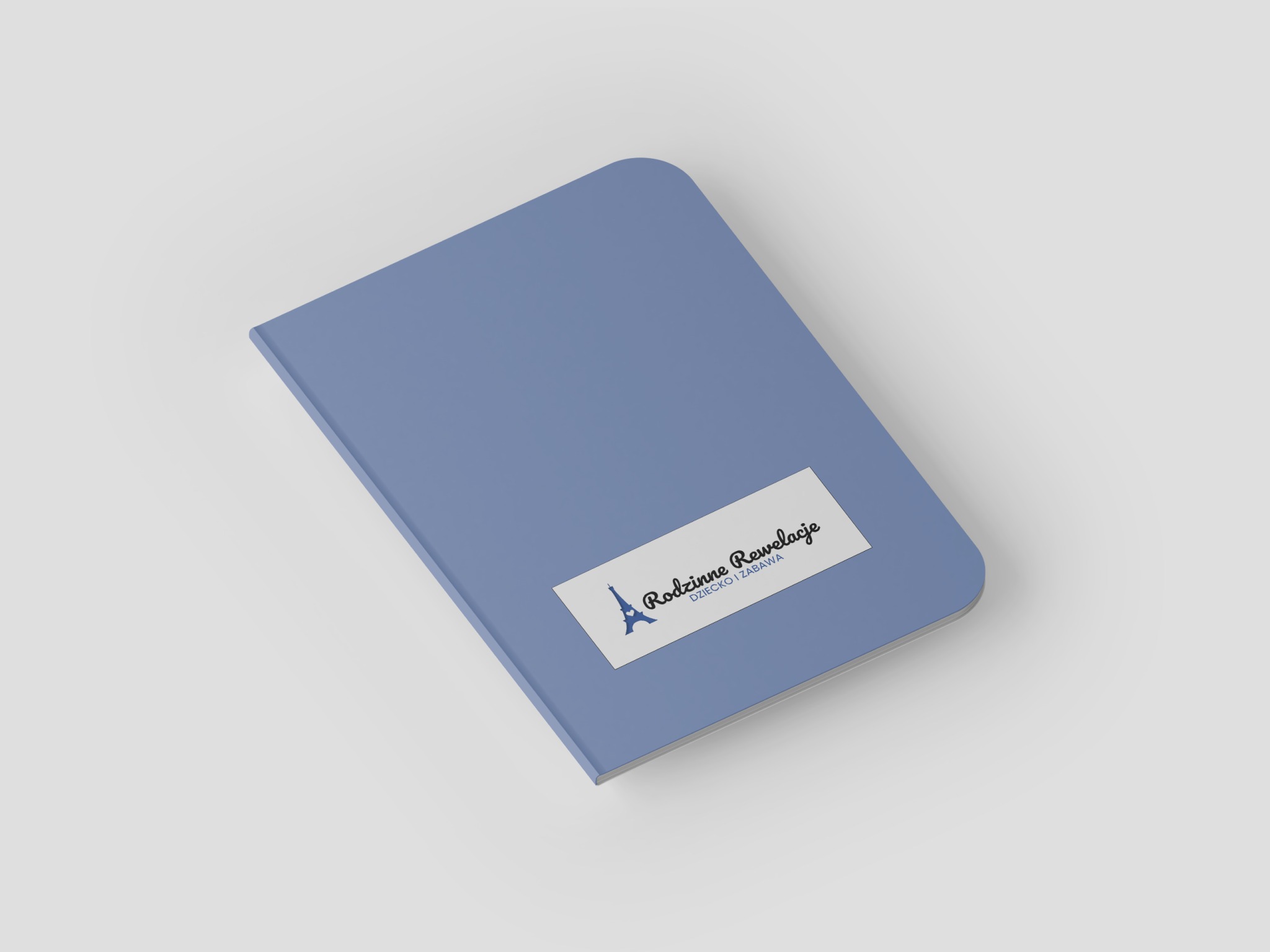 Niebieski notatnik z zaokrąglonymi rogami, na którym umieszczono białą naklejkę z logo przedstawiającym wieżę Eiffla i napisem 'Rodzinne Rewelacje DZIECKO I ZABAWA'.