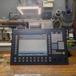 Panel sterowania CNC Siemens Sinumerik na warsztatowym stole we Wrocławiu, otoczony narzędziami i sprzętem elektronicznym, wyświetlający komunikat 'Czekaj na połączenie z NC/PLC'.