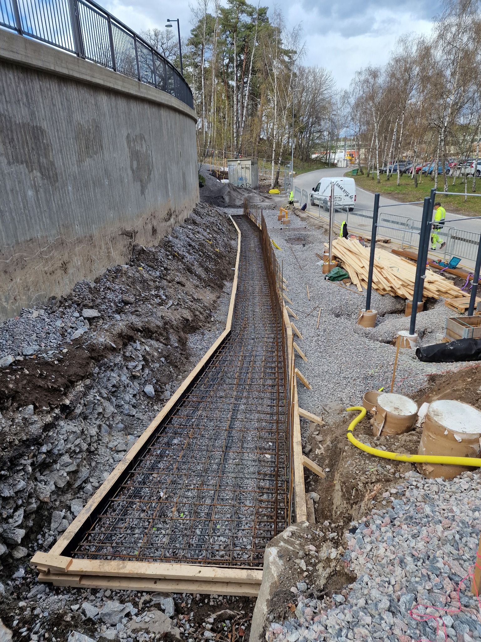 Zbrojenie fundamentu pod mur oporowy z drewnianym szalunkiem, widok z góry. Elementy konstrukcyjne, gruz i żwir na placu budowy. Robocze ujęcie z budowy.