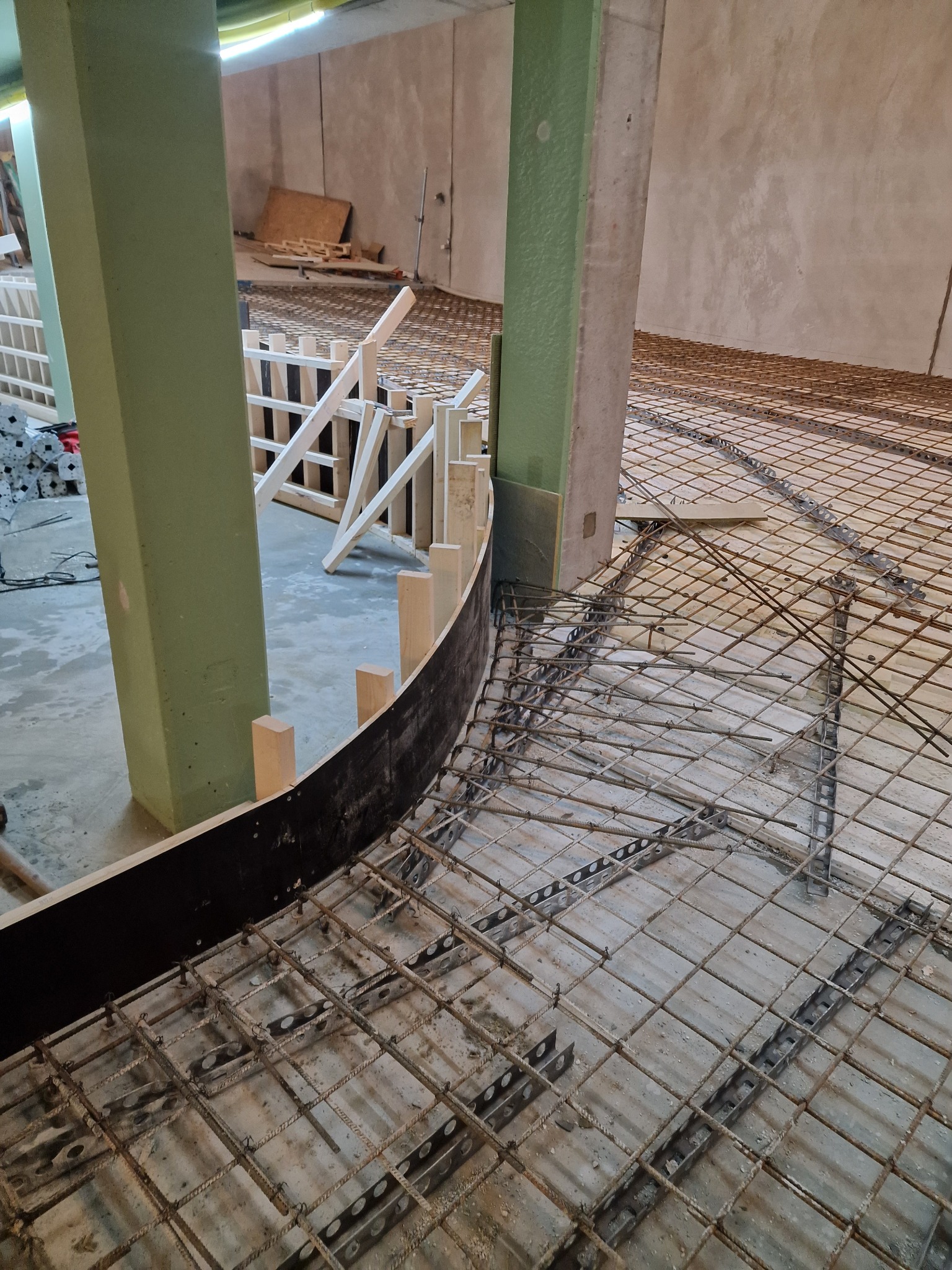 Zbrojenie pod wylewkę fundamentów z zakrzywioną szalunką i słupami nośnymi, widoczne detale konstrukcyjne i betonowe podłoże.