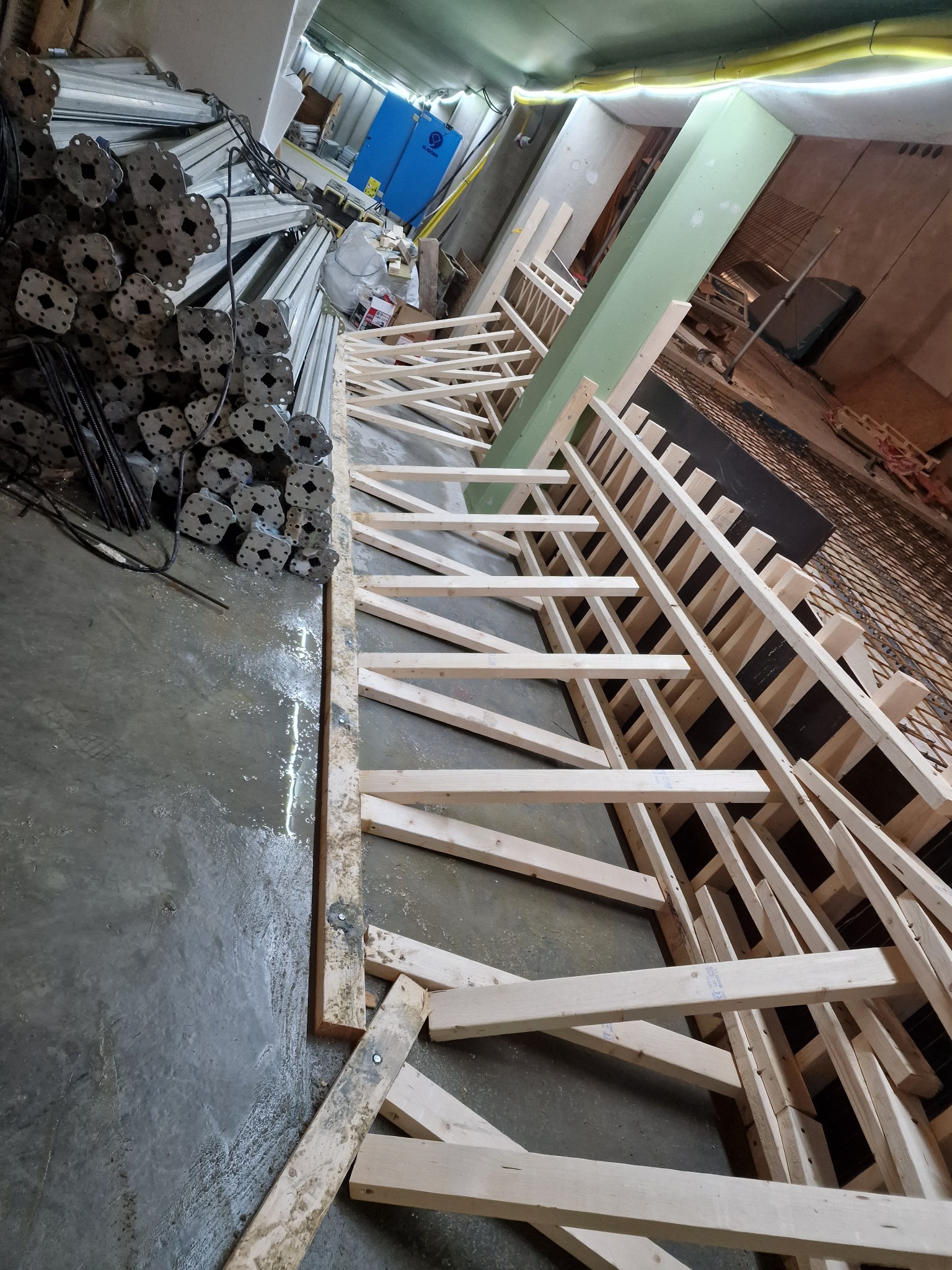 Szalunek drewniany zbrojenia fundamentów w Tomaszowicach, przygotowany do wylania betonu. W tle widoczne podpory i materiały budowlane.