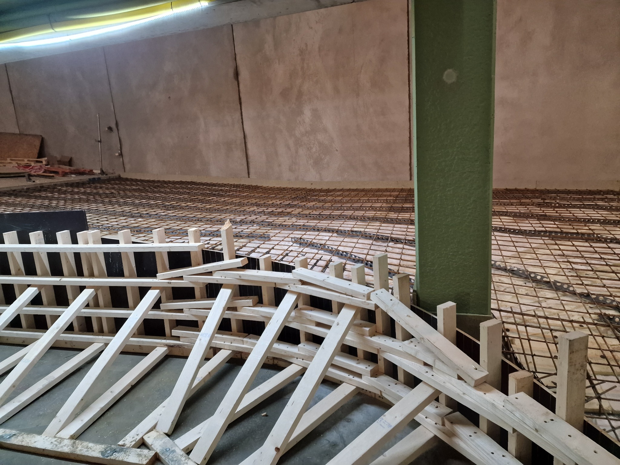 Zbrojenie pod wylewkę z drewnianym szalunkiem w surowym wnętrzu. Widoczne siatki zbrojeniowe i konstrukcja z desek, przygotowane do betonowania.