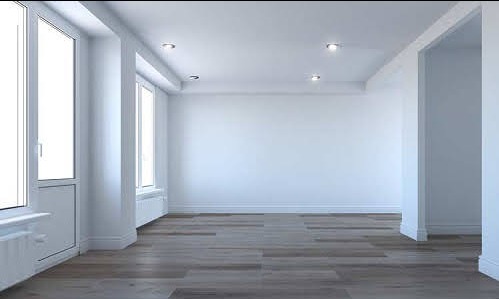 Pusty, jasny pokój z drewnianą podłogą, białymi ścianami i oknami, przygotowany do prac wykończeniowych, widoczne listwy przypodłogowe i oświetlenie punktowe.