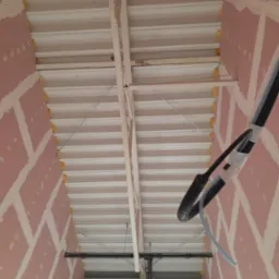 Poddasze w trakcie ocieplania z widoczną konstrukcją, izolacją między krokwiami i częściowo wykończoną płytą gipsową na ścianach.