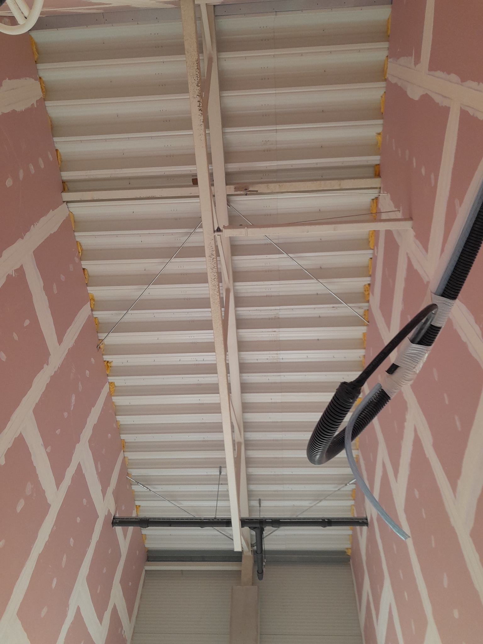 Poddasze w trakcie ocieplania z widoczną konstrukcją, izolacją między krokwiami i częściowo wykończoną płytą gipsową na ścianach.