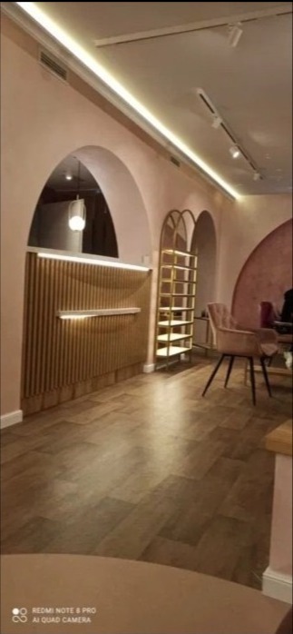 Wnętrze biura z łukami w odcieniach różu, drewnianą ladą z podświetleniem LED, złotym regałem i parkietem w jodełkę.