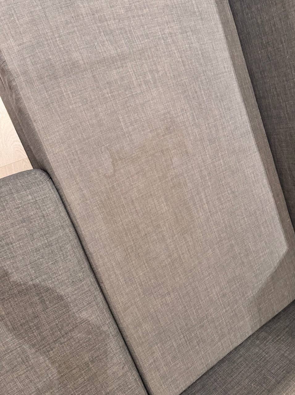 Szary, teksturowany narożnik sofy z widocznym jaśniejszym plamą na siedzisku, sugerującym potrzebę czyszczenia tapicerki.