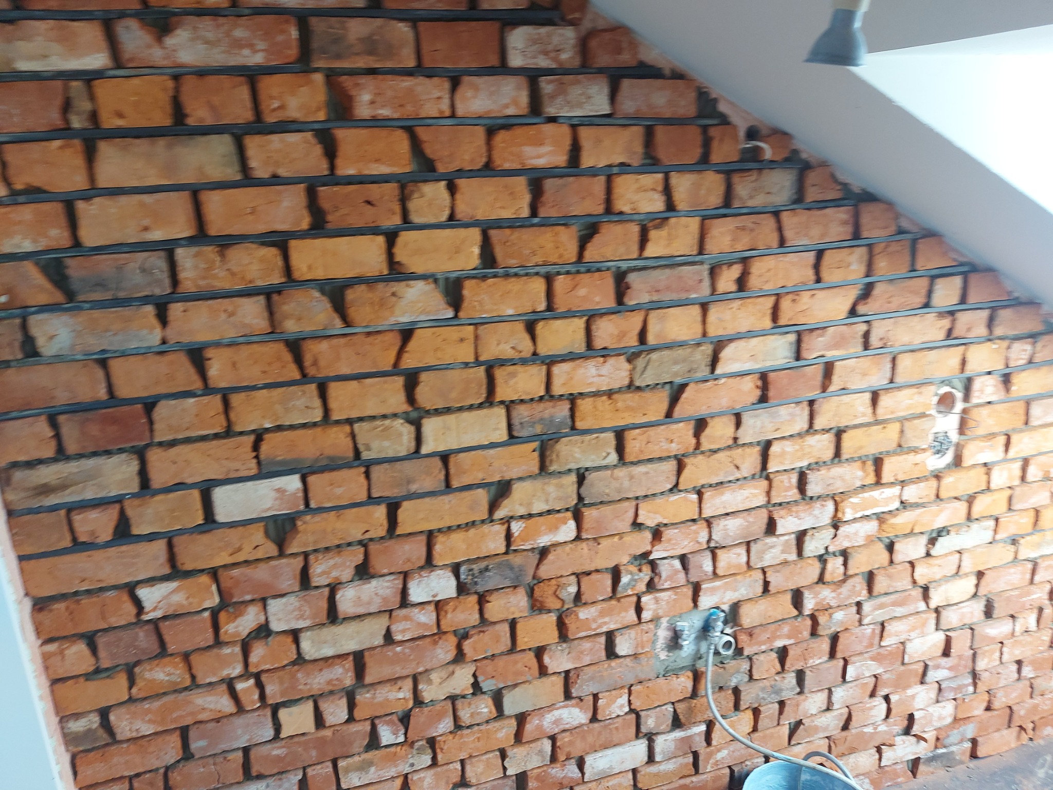 Ściana z cegły klinkierowej w trakcie budowy z widocznymi poziomymi spoinami i instalacją hydrauliczną.