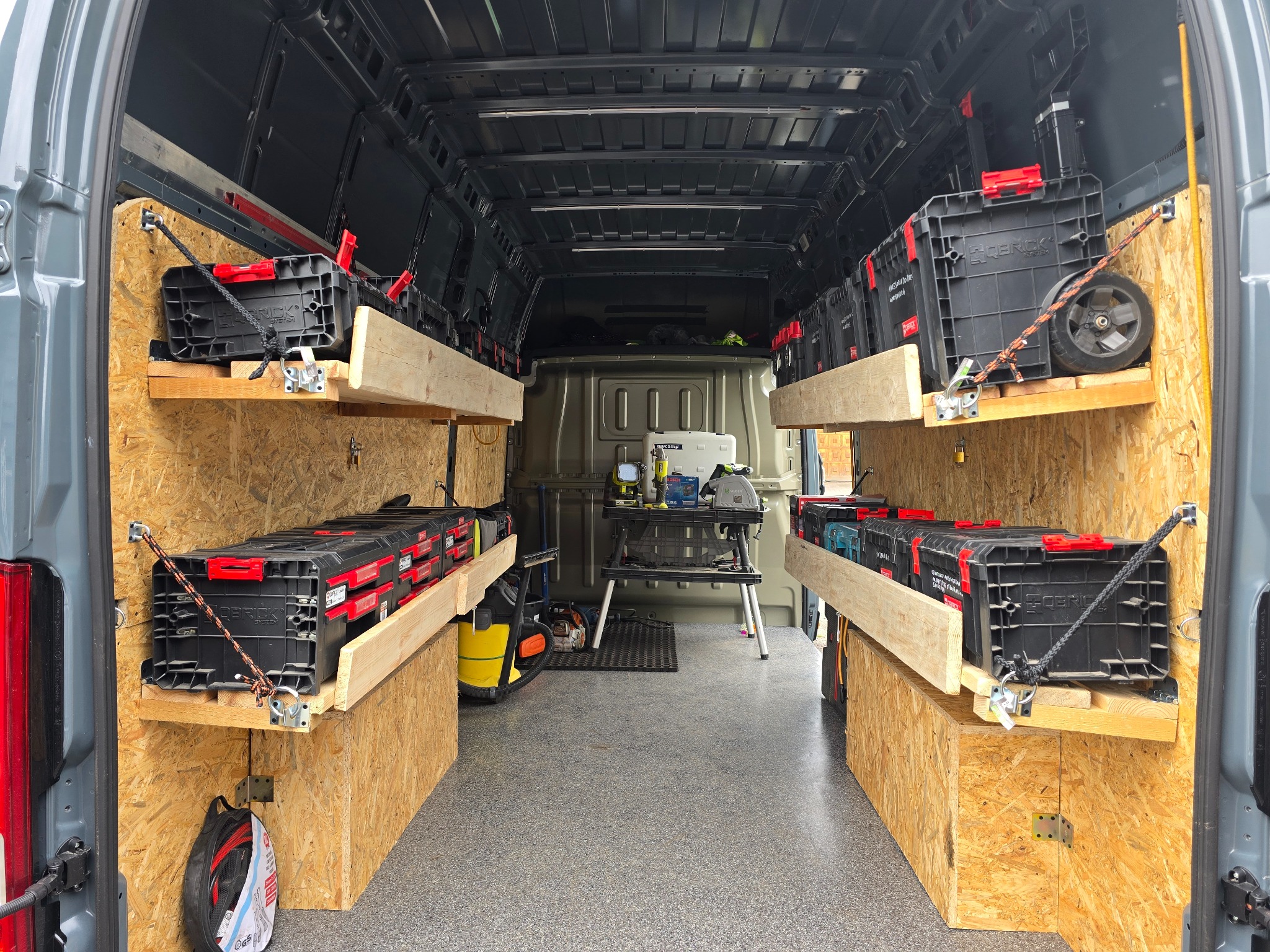Wnętrze szarego busa z zabudową warsztatową: półki z płyty OSB, skrzynki narzędziowe QBRICK, stół roboczy i narzędzia. Gotowe do transportu i pracy u klienta.