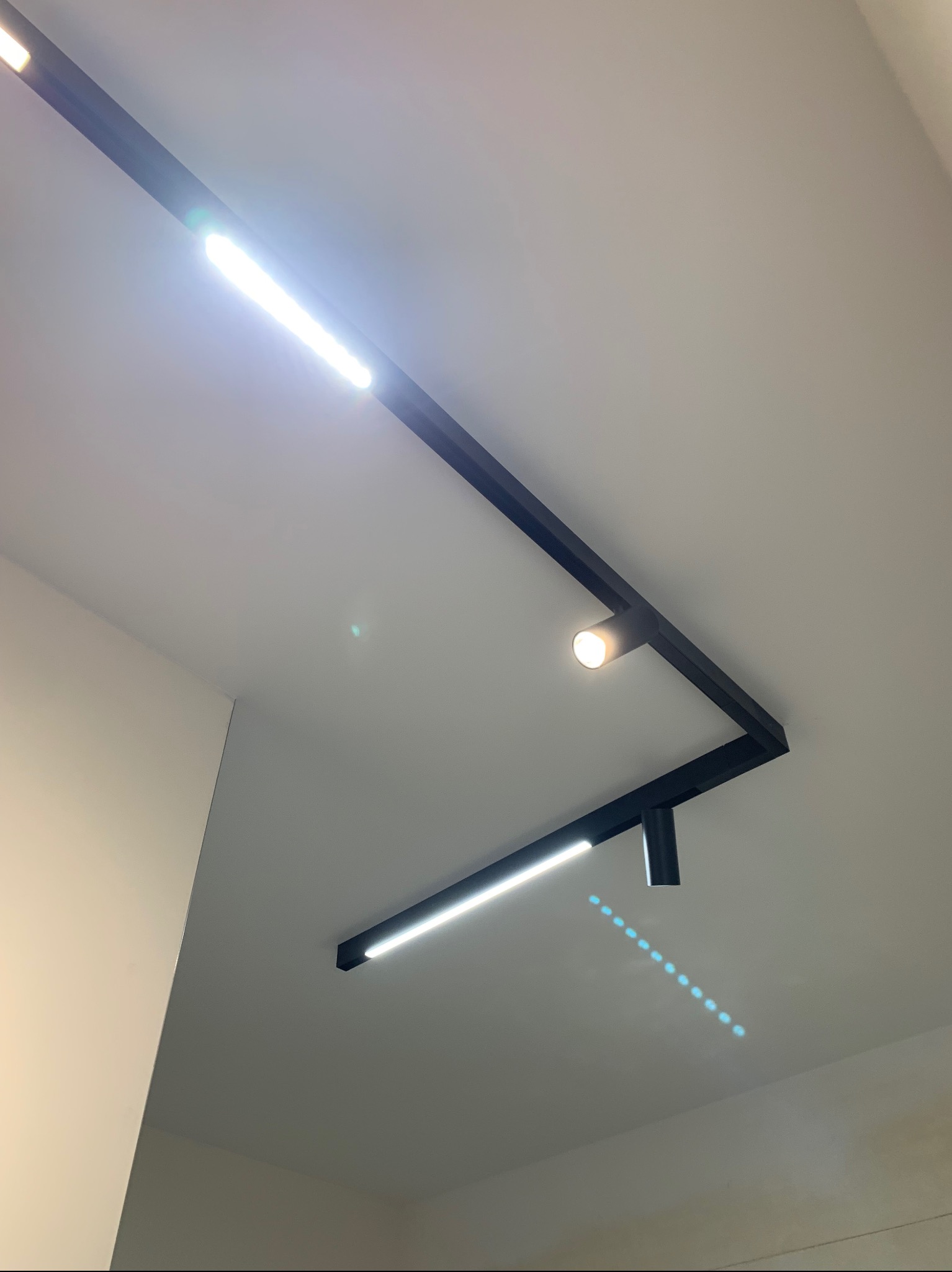 Czarna, geometryczna oprawa oświetleniowa z dwoma liniowymi źródłami światła LED i jednym punktowym, zamontowana na suficie.