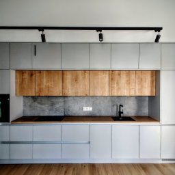 Jest Poziom - Nowoczesna kuchnia z szarymi szafkami, drewnianymi akcentami i czarną armaturą, oświetlona reflektorami na szynoprzewodzie.