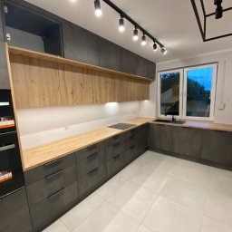 Jest Poziom - Nowoczesna kuchnia w odcieniach szarości z drewnianymi akcentami, oświetleniem punktowym i dużym oknem z widokiem na zieleń.