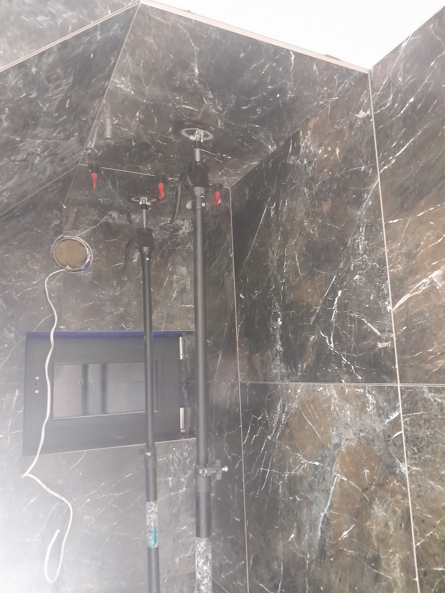 Montaż płytek marmurowych na ścianie z użyciem podpór teleskopowych, widoczna instalacja elektryczna i otwór na gniazdko.