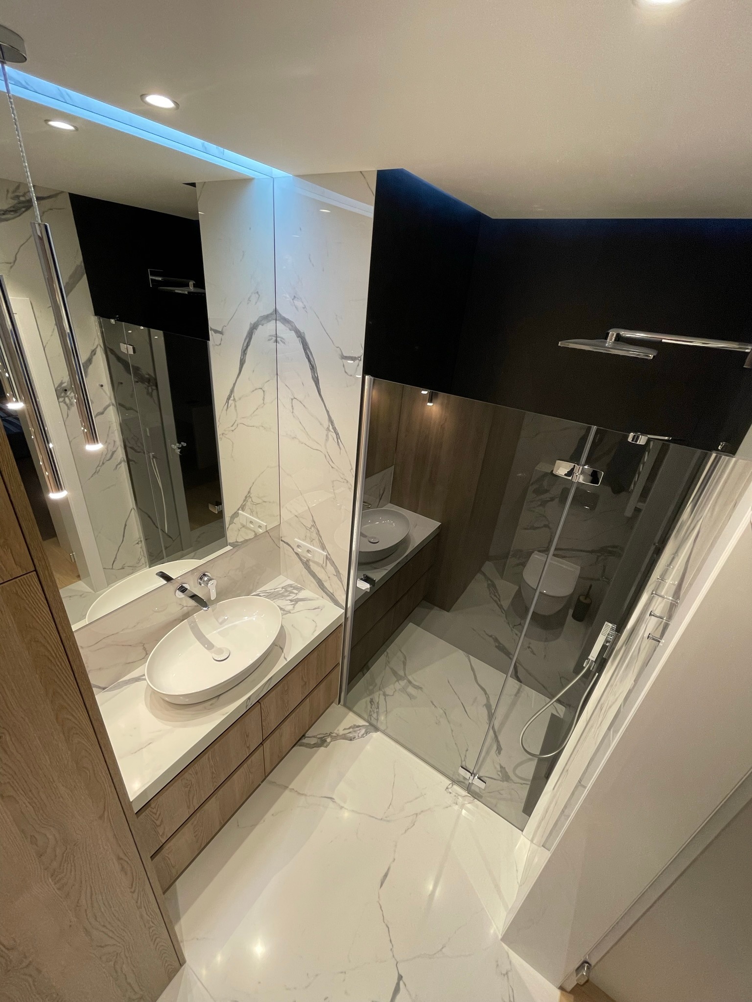 Nowoczesna łazienka z kabiną prysznicową typu walk-in, umywalką nablatową na drewnianej szafce i marmurowymi płytkami na ścianach i podłodze, oświetlenie punktowe i wiszące lampy.