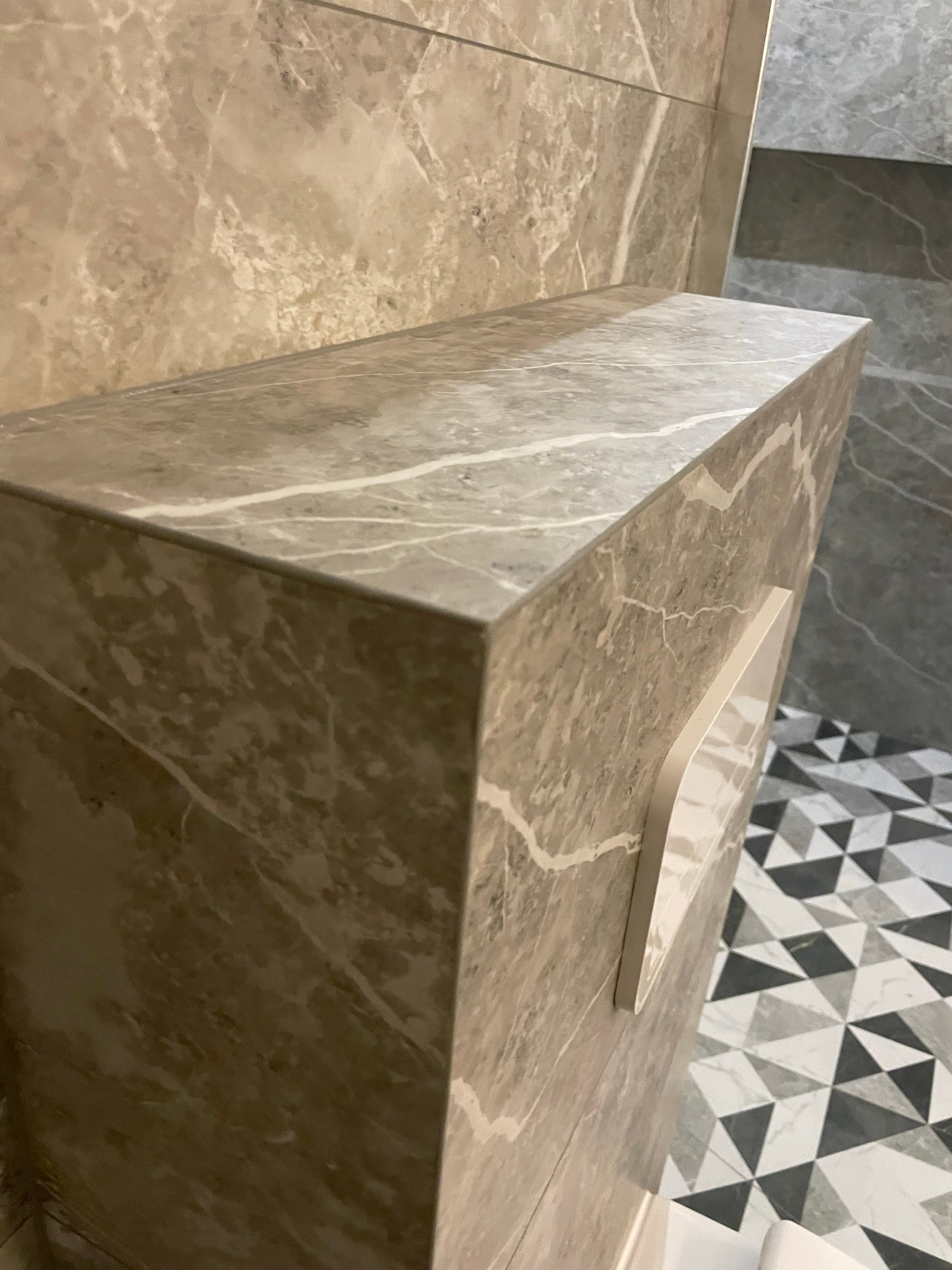 Wykończona łazienka: Detal umywalki z blatem z płytek imitujących marmur, dopasowanych do płytek ściennych, z widocznym fragmentem podłogi z geometrycznym wzorem.