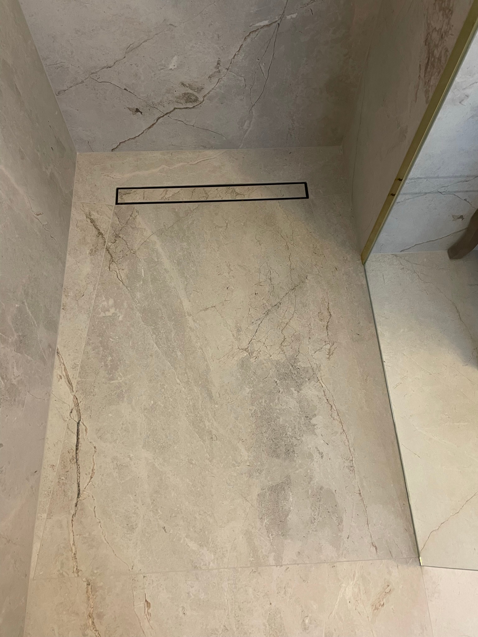 Beżowa łazienka wykończona marmurowymi płytkami z czarnym odpływem liniowym pod prysznicem.