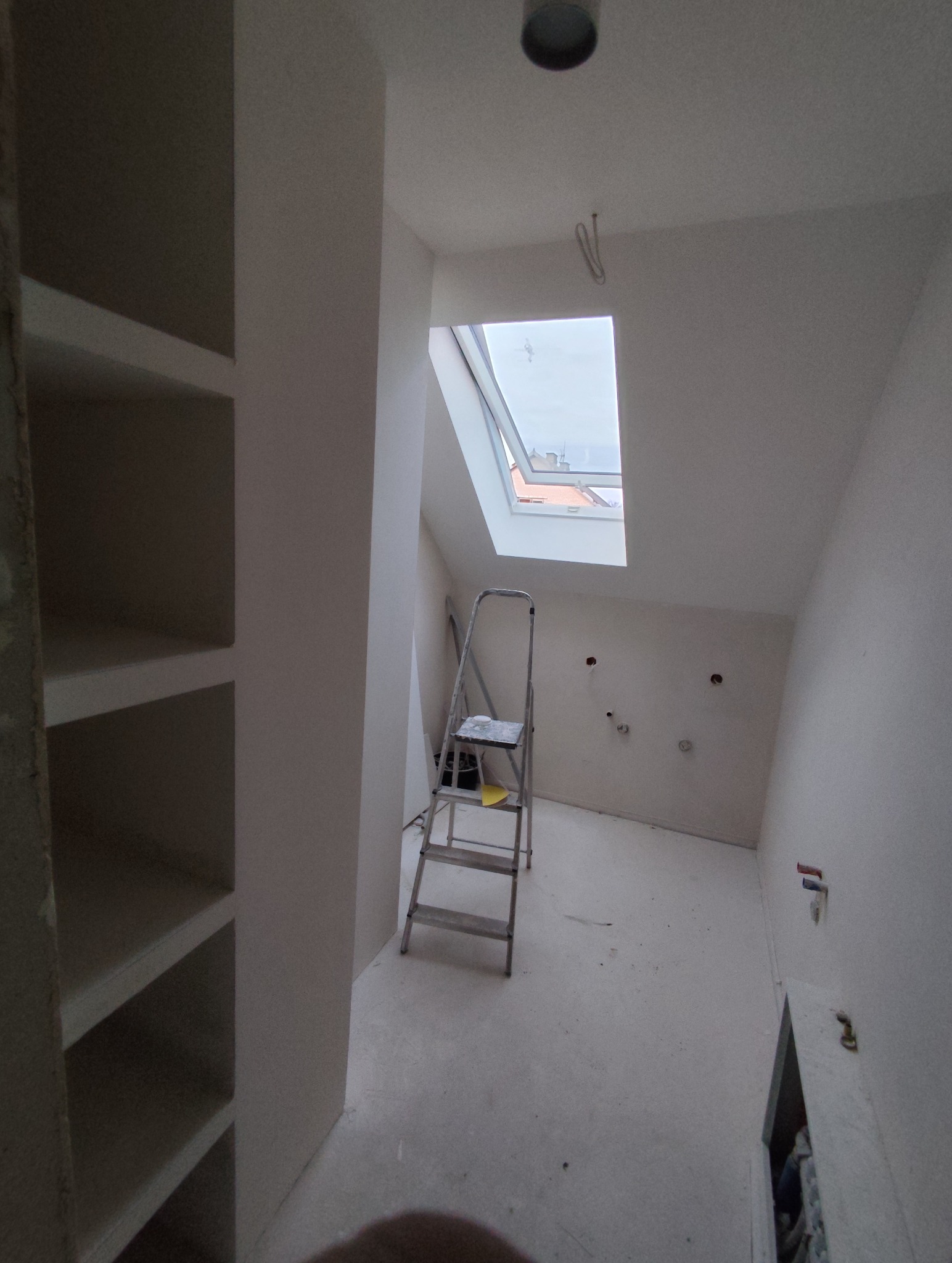Poddasze po szpachlowaniu, widoczna drabina, okno dachowe i przygotowane ściany pod malowanie. W tle zabudowa regałowa.