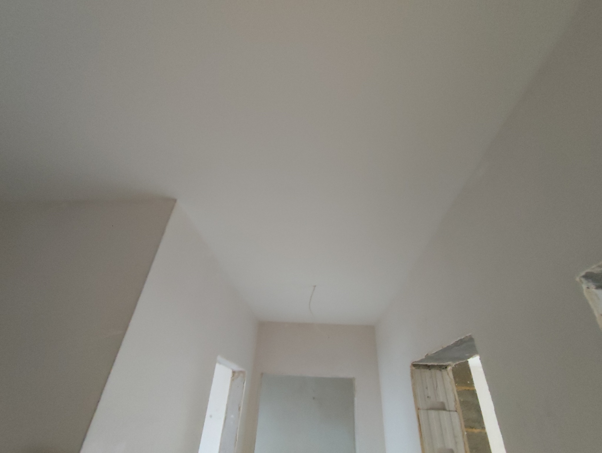 Wnętrze w trakcie wykończenia: białe ściany i sufit po szpachlowaniu, widoczne otwory drzwiowe z surowymi ościeżami. Minimalistyczny kadr, neutralne oświetlenie.