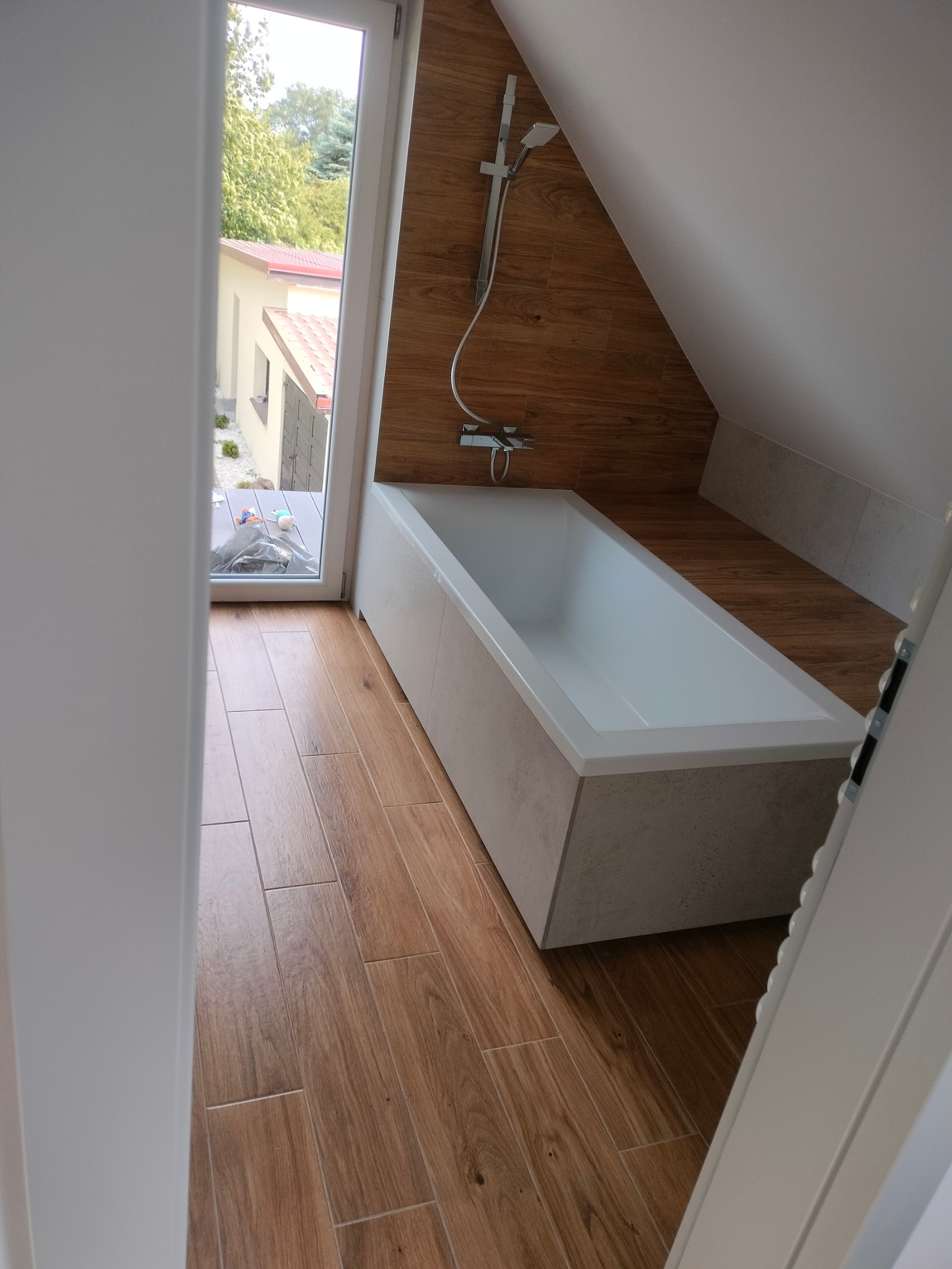 Nowoczesna łazienka na poddaszu z wanną, drewnopodobną glazurą i oknem z widokiem na ogród. Ukończony remont, estetyczne wykończenie.