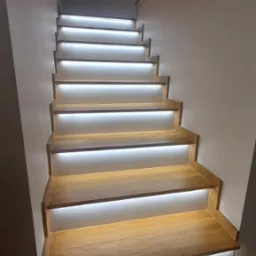 Nowoczesne schody drewniane z podświetleniem LED, widok z dołu, minimalistyczne wykończenie.