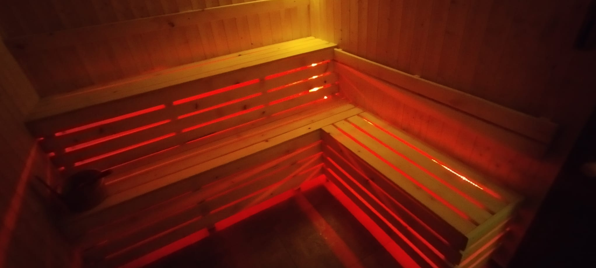 Wnętrze sauny z drewnianymi ławkami, oświetlone czerwonym światłem, widok z góry.