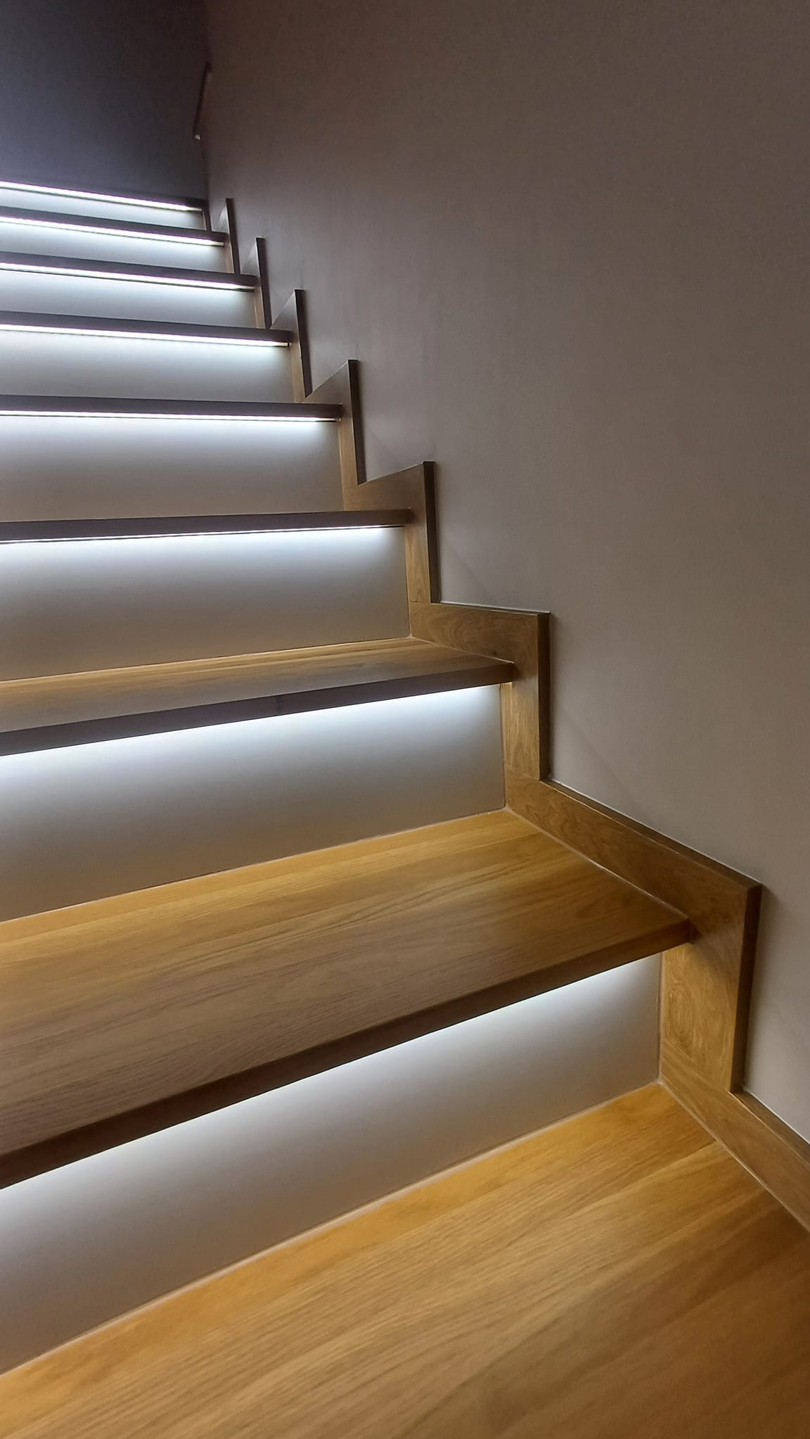 Nowoczesne, drewniane schody z podświetleniem LED, widok z dołu, ukazujący eleganckie wykończenie i subtelne oświetlenie stopni.