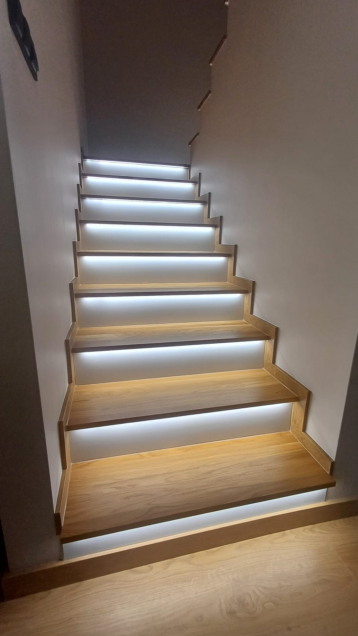 Nowoczesne schody drewniane z podświetleniem LED, widok z dołu, minimalistyczne wykończenie.