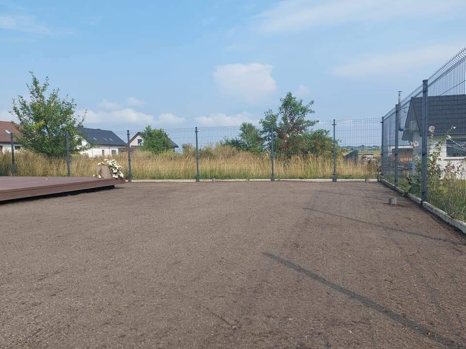 Przygotowany teren pod trawnik, wyrównana ziemia z widocznym ogrodzeniem panelowym i fragmentem tarasu w tle.