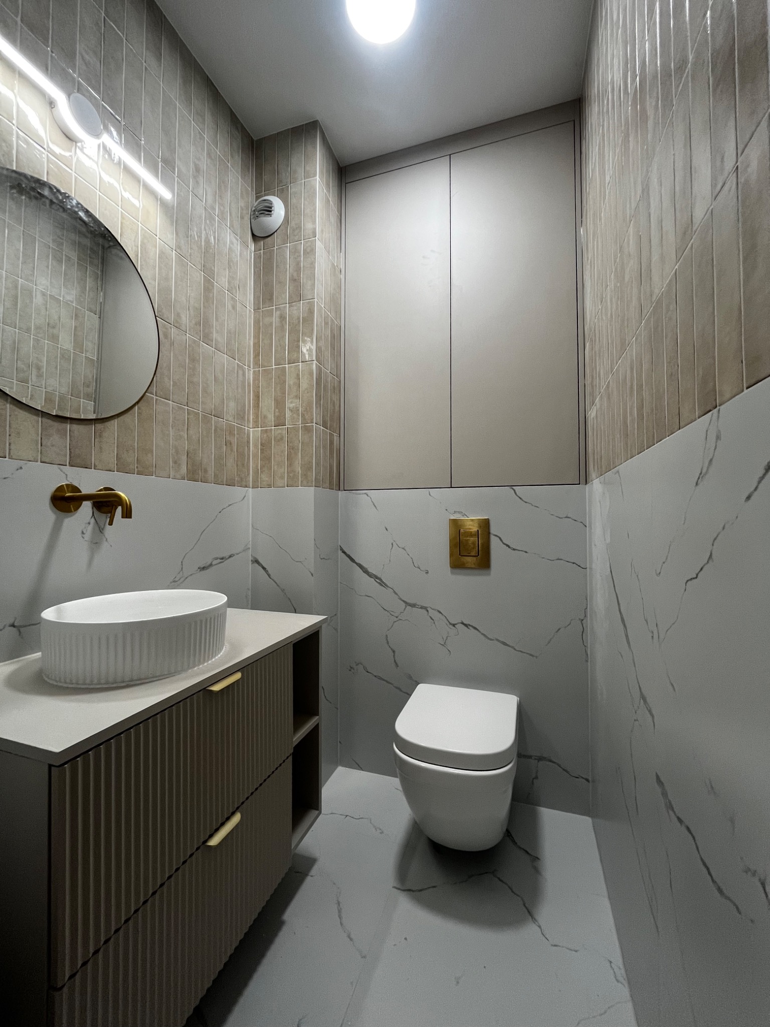 Wykończona łazienka w Gdańsku z umywalką nablatową, armaturą w kolorze złotym, podwieszaną toaletą i płytkami imitującymi marmur.