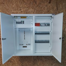 Elecrtrovia - Otwarta, biała skrzynka elektryczna z zainstalowanymi bezpiecznikami i elementami montażowymi, zamontowana na ścianie z płyty OSB.